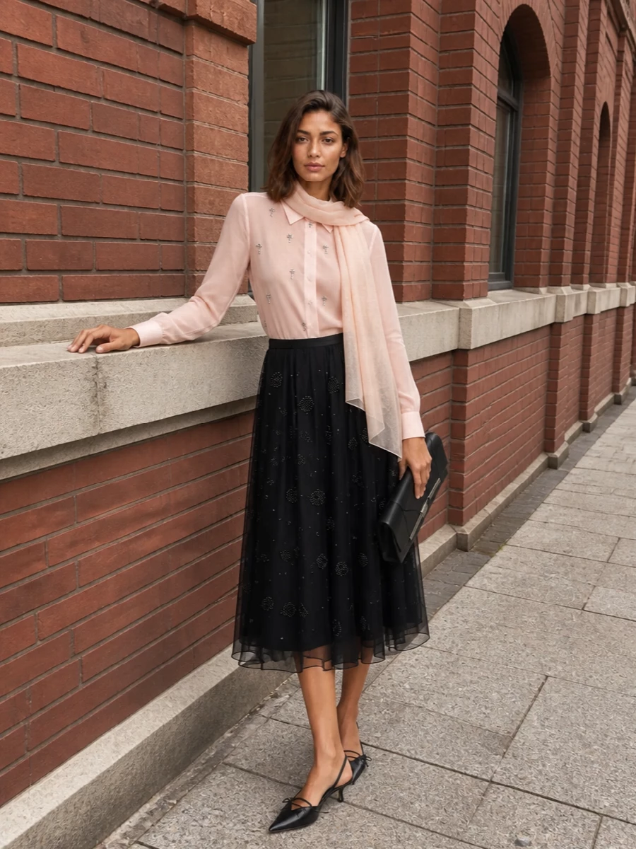 A sheer blush embellished shirt softens the drama of the beaded black midi skirt, creating a romantic, candlelit palette that still feels sharply tailored. Pointed black kitten heels and a structured black clutch keep the line clean and formal, letting texture and subtle sparkle carry the story. The blush wrap ties the tones together, giving you an extra whisper of coverage for warm summer evenings.