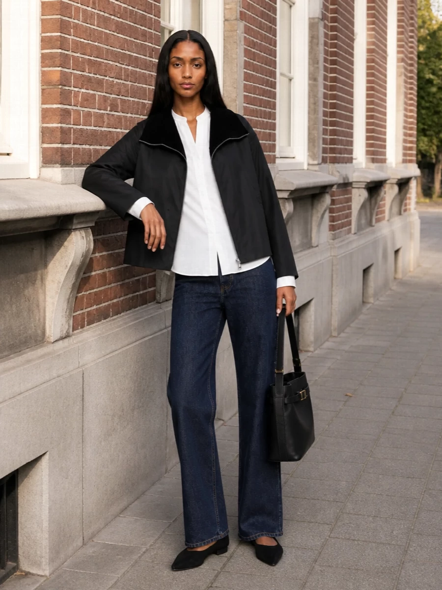 I am keeping this firmly in Totême’s city-uniform space: a cropped, sculpted black jacket over a crisp collarless white shirt, long dark denim and sharp black flats. The proportions stay relaxed up top and long through the leg, with the structured black bucket bag reinforcing the clean, architectural mood. I chose the shirt and jean route over a dress to echo the source styling and preserve that understated, off-duty tailoring balance between ease and precision.