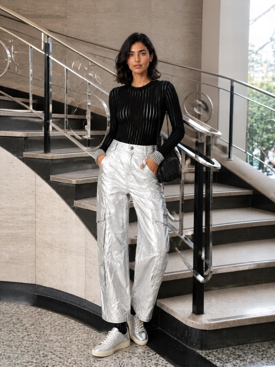 High-rise metallic cargos become the hero, grounded with a sheer, body-skimming black knit that flashes crystal only at the cuffs. Silver sneakers keep the energy club-ready yet easy to move in, while a glossy black crossbody and rhinestone socks pull the shine into a tight, monochrome night-out story. It is pure downtown Y2K attitude with a streamlined, future-facing silhouette.