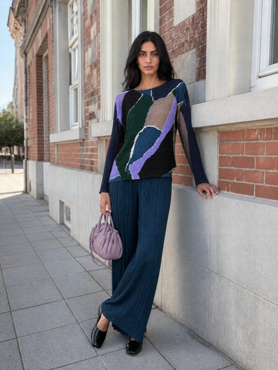 Pleats Please pleating meets an art-gallery palette here, with the printed top floating over deep teal wide legs for movement that feels romantic and composed rather than busy. Glossy black flats keep the line clean and modern, while the lilac mini bag quietly pulls out the softer tones in the print for a considered, boho-leaning finish.