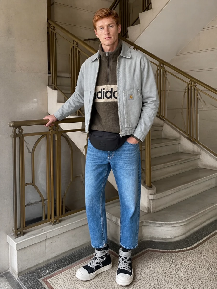 Carhartt WIP’s washed grey jacket sits over an olive Adidas fleece and cropped Acne denim for a low-key, street-led take on workwear. Rick Owens DRKSHDW high-tops and a sleek Moncler belt bag sharpen the proportions, giving the cropped jacket and jeans a more directional, city-ready attitude while staying easy to wear in colder weather.