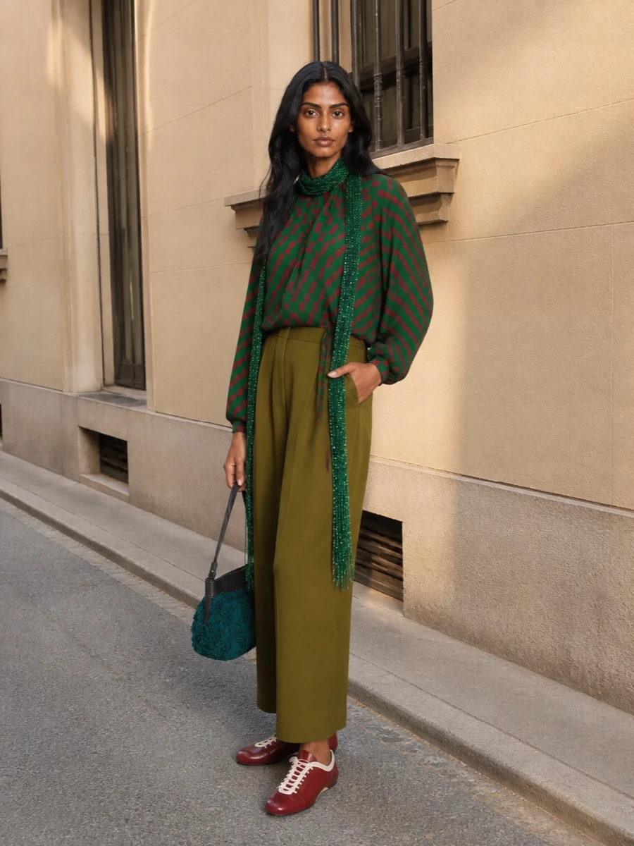 A vivid Dries blouse sits against fluid olive wide-legs, letting the print read strong but not shouty. Deep red flats and an emerald rosette bag carry the color story in quieter notes, so the whole outfit feels artful, relaxed and intentionally composed for summer days that drift into night.