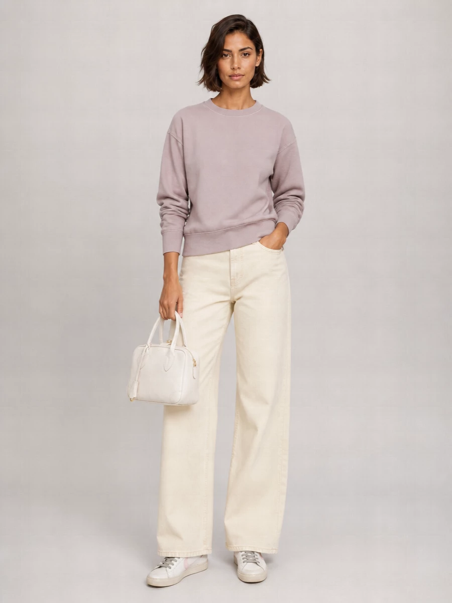 A dusty mauve sweatshirt and buttercream wide-leg jeans pick up the blush and off-white tones of the sneakers for an easy, soft-focus palette. The high-rise, full-length denim keeps the proportions long and relaxed, letting the worn-in sneakers feel intentional rather than too casual. A chalky white mini bag finishes it with a tidy, modern contrast against all the gentle neutrals.