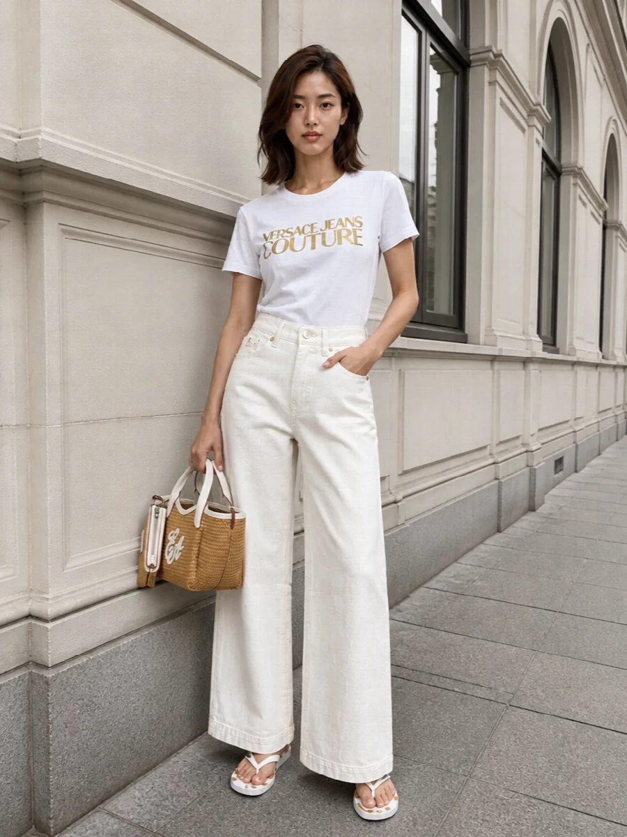 This outfit takes the Versace flip-flops out of pure pool territory and into chic beach-city crossover, pairing them with a clean white and gold logo tee and off-white wide-leg denim. The palette stays in warm whites and soft neutrals with a single hit of gold, so the branded details feel intentional rather than loud. A woven mini tote finishes it with a subtle Riviera tone that still feels practical for holiday errands and strolls along the promenade.