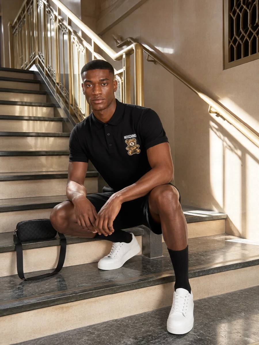 A black Moschino polo meets tailored black cargo shorts for a clean, graphic take on casual city dressing. Off-white Moschino sneakers break up the monochrome and keep it fresh, while a slim black belt and streamlined Gucci sling bag finish the outfit with quiet designer detail. It is an easy, go-anywhere warm-weather uniform that still reads considered and put together.