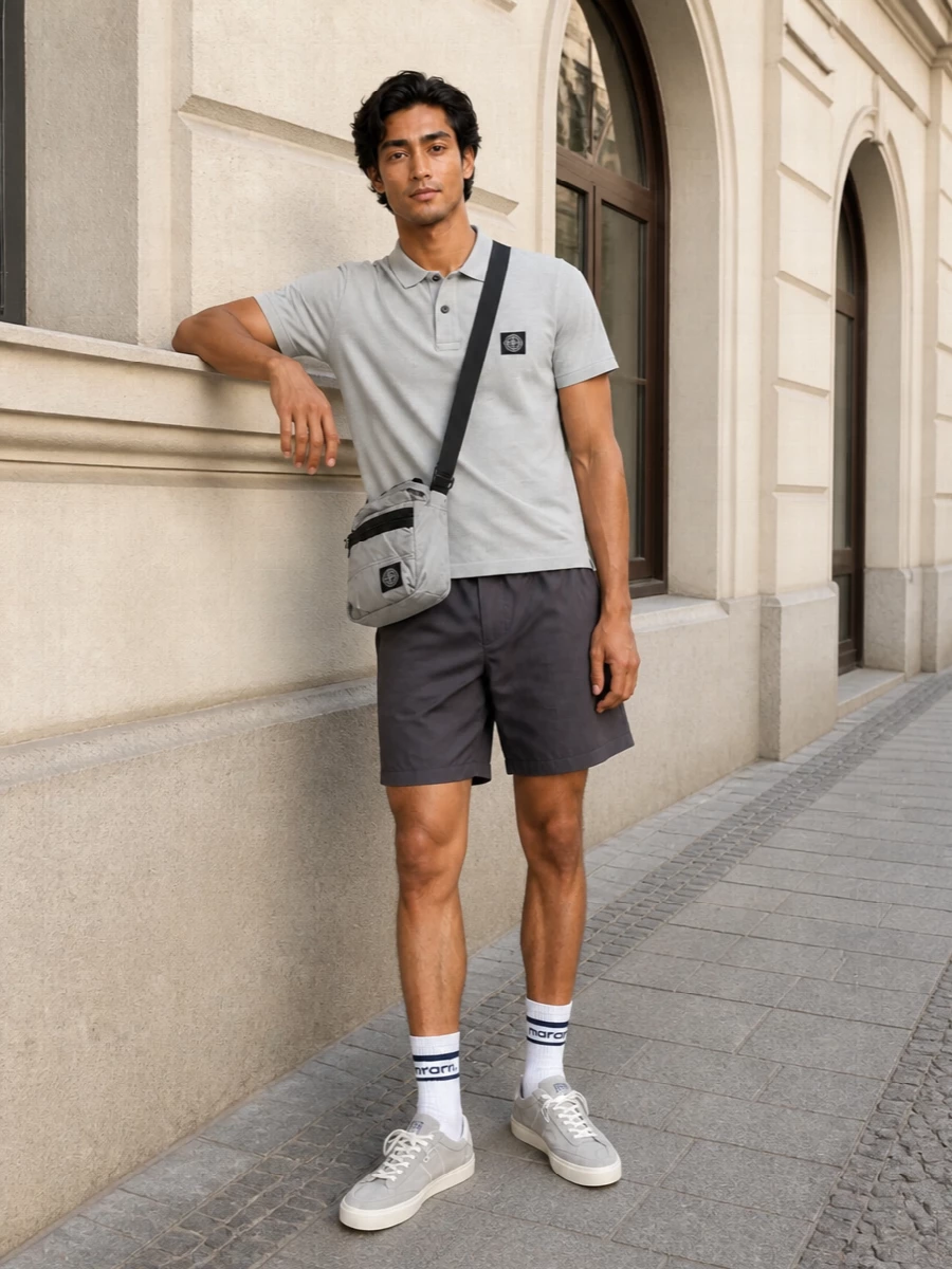 Soft grey on top and charcoal on the bottom keep this Stone Island set clean, graphic and easy for warm city days. Light grey suede sneakers and a matching technical crossbody hold the palette in a tight, modern neutral range while staying relaxed. It is a quietly branded street-sport uniform that feels considered without ever looking overthought.