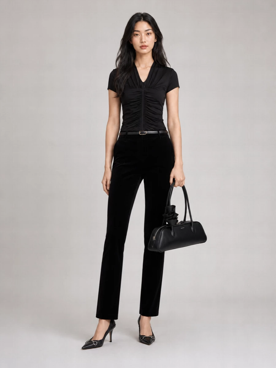 A ruched black blouse sits against sleek velvet tailoring, creating a monochrome line that feels quietly sensual rather than overt. The sharp pump and sculptural shoulder bag bring just enough shine and structure, so the texture mix does the talking. It is an evening city uniform that reads considered from every angle.