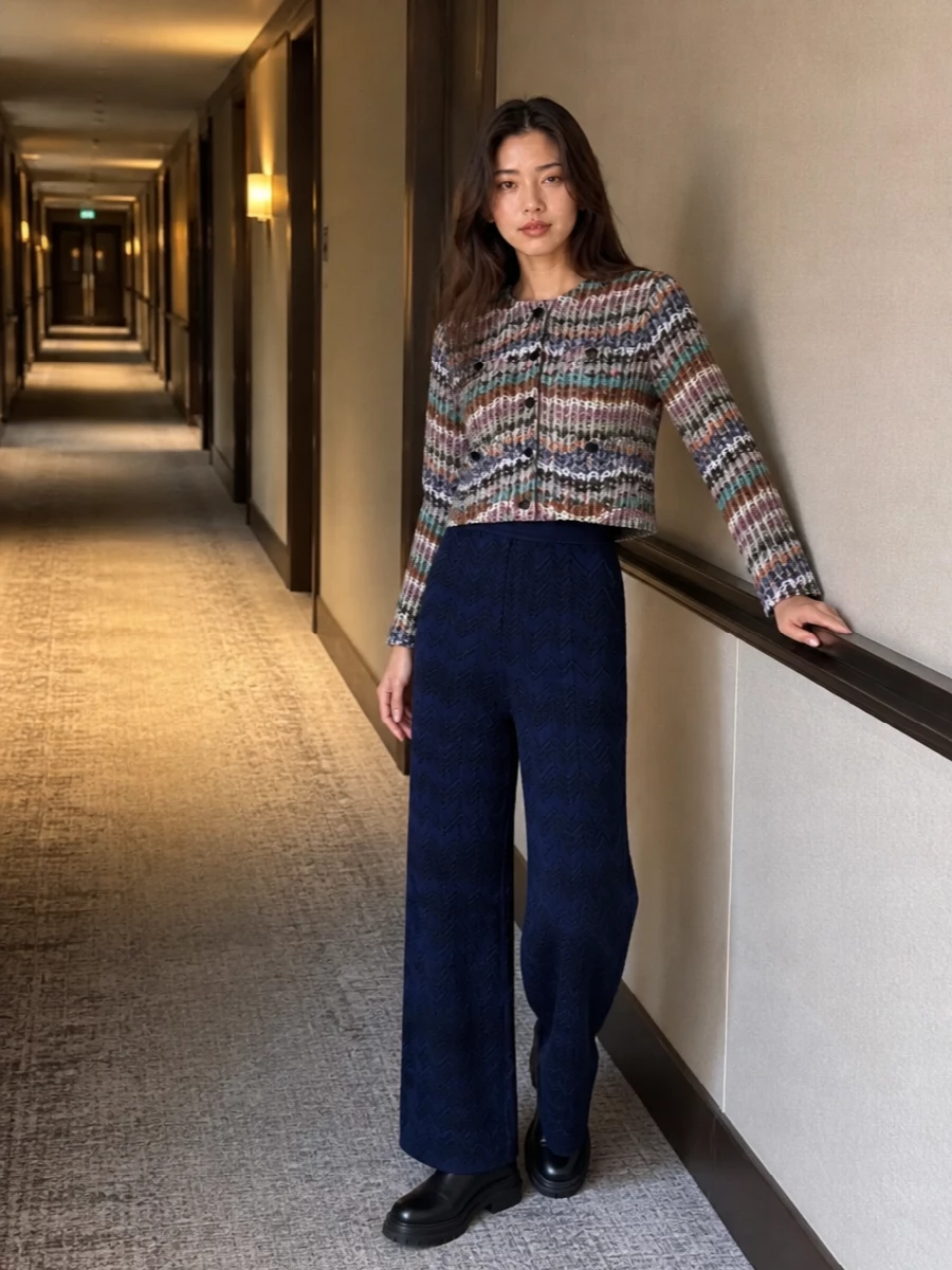 A cropped Missoni cardigan sits cleanly over deep navy knit trousers, letting the multicolour texture stay the focus against a calm, elongated base. Chunky black ankle boots and a structured chestnut top-handle bag bring just enough city polish to keep the knit pairing from feeling too relaxed, while the softly patterned scarf ties the warm and cool tones together. The result is a quietly graphic, boho-preppy mix that feels refined but easy for cooler days.