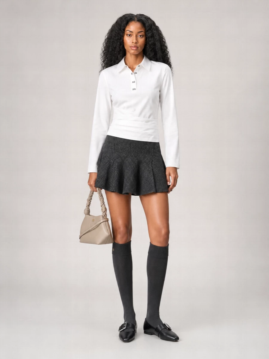 A clean white collared top meets a sharp charcoal pinstripe mini for a Scandinavian take on preppy. Black pointed flats and charcoal knee-high socks ground the swingy proportions without losing ease. A small taupe crossbody keeps the whole mix quietly structured and city ready.