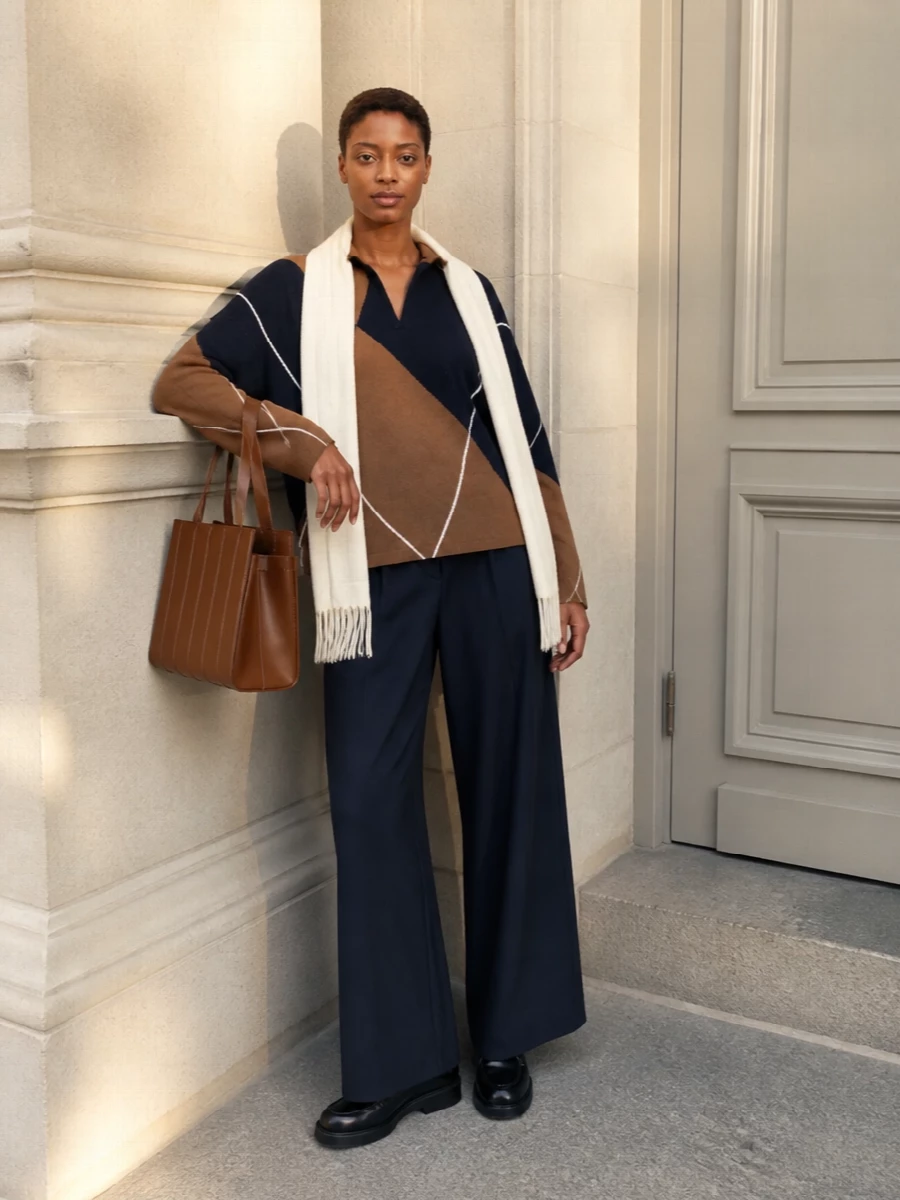 Deep navy and camel fall into an easy conversation here, with the graphic rugby knit grounded by fluid navy wide-leg trousers. A structured chestnut tote and black lace-up derbies sharpen the softness, keeping the outfit casual enough for errands yet composed for a relaxed office. The ivory scarf lightens everything at the face, echoing the sweater’s fine white lines for a quiet but intentional finish.