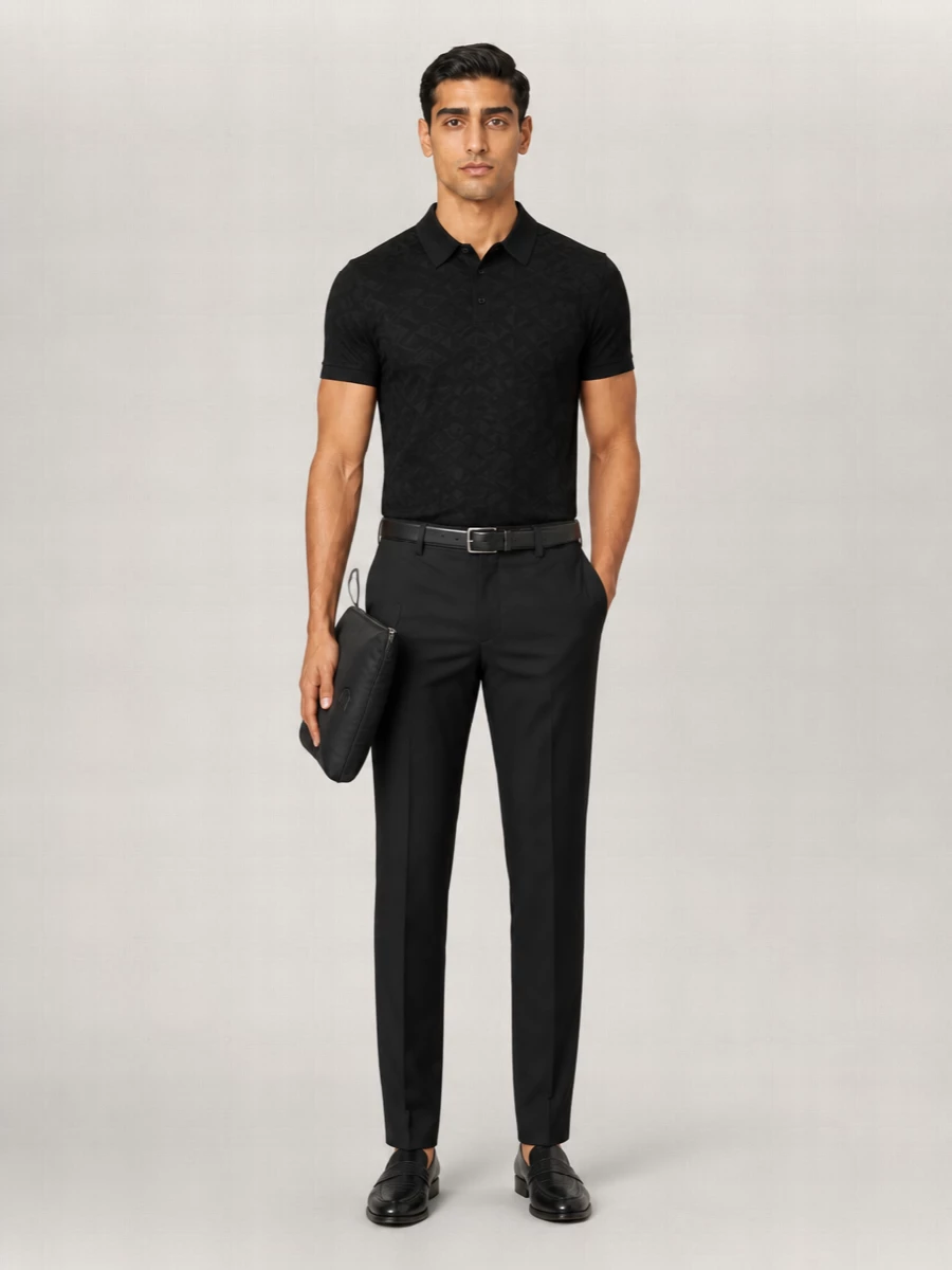 A black jacquard polo sits over slim black suit trousers for a monochrome take on Italian tailoring that feels polished yet quietly relaxed. Textured loafers and a discreet black belt keep the line sharp without tipping into full formalwear. The result is an easy city uniform that moves smoothly from client lunch to late dinner reservations.