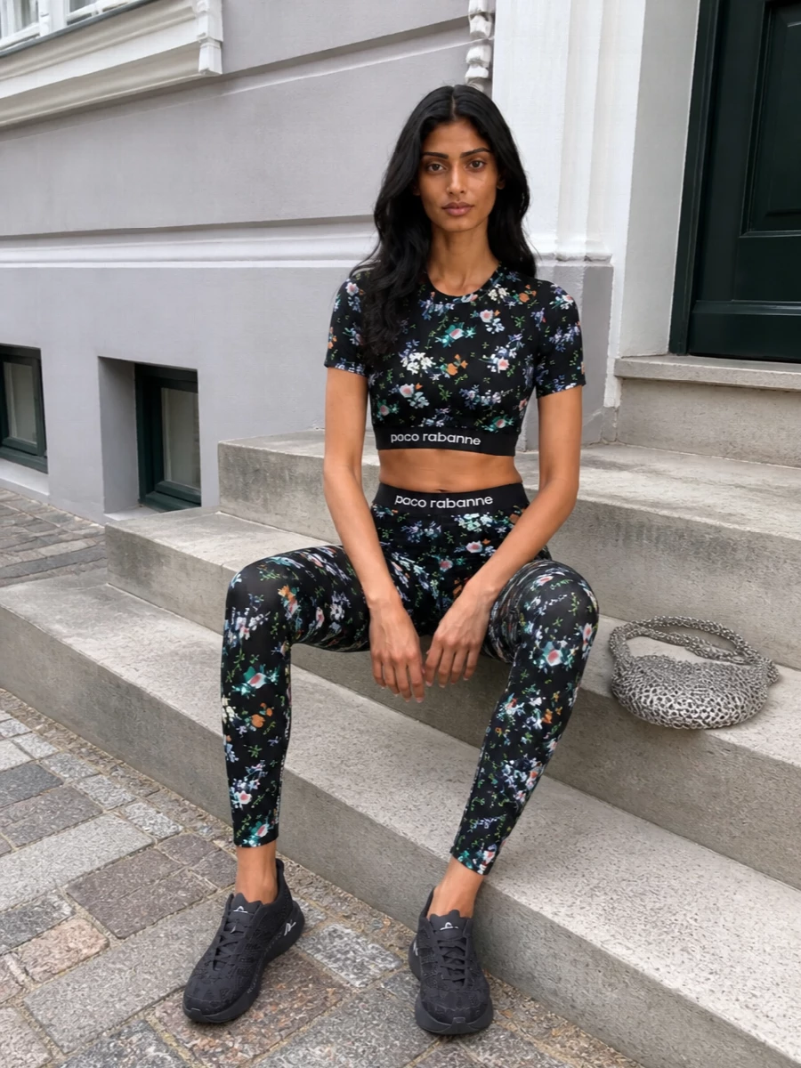 Paco Rabanne’s dark floral set leans into a sleek, body‑con silhouette that feels equal parts gym‑ready and nightlife‑charged. Graphic runners keep the mood grounded and functional, while the silver chainmail bag brings that unmistakable Paco metal shimmer for an easy studio‑to‑after‑hours transition.