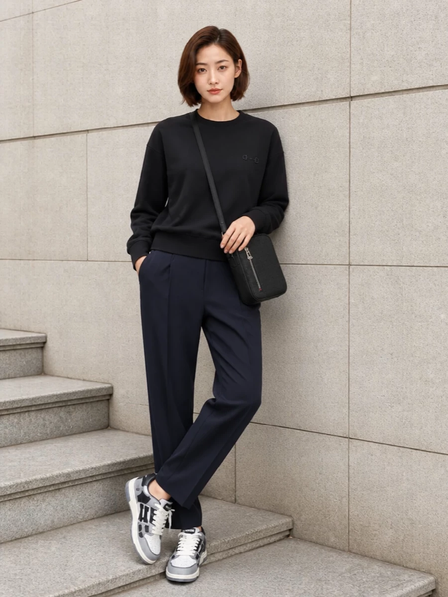 Ink navy track trousers meet a sharp black crew sweatshirt for a clean, sport-driven base that feels relaxed but intentional. Graphic monochrome sneakers keep the palette tight while adding street energy, and a compact black crossbody finishes it with low-key polish that still reads ready for movement. It is a modern, luxury take on track dressing that works from coffee runs to casual city days.