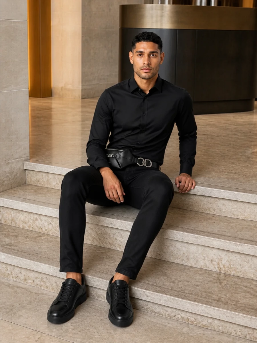 An all-black, slim-lined take on Italian city dressing, this pairing keeps the focus on clean structure and quiet details. The regular-cut shirt and mid-rise jeans track each other closely, so the proportions stay sharp whether you are standing or seated. Textured black sneakers and a precise belt and waist bag keep everything grounded in modern streetwear polish without diluting the tailored edge.