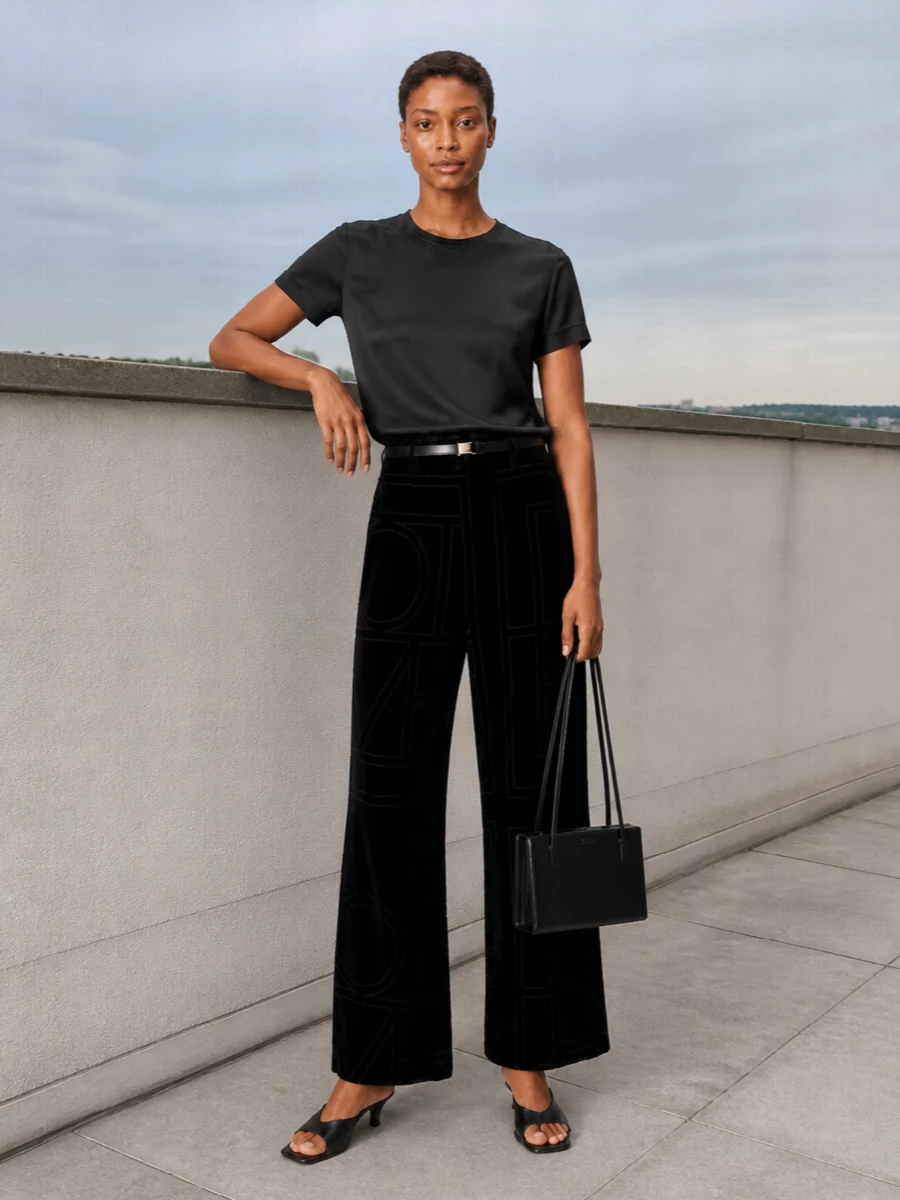 A study in black textures, this pairing lets the geometric velvet trouser take the lead against a quietly lustrous satin top. A low kitten-heel sandal and slim belt refine the proportions, while a sharp rectangular shoulder bag finishes the silhouette with clean, evening-ready precision. The result is modern and composed, ideal for gallery nights or intimate dinners where detail reveals itself up close.