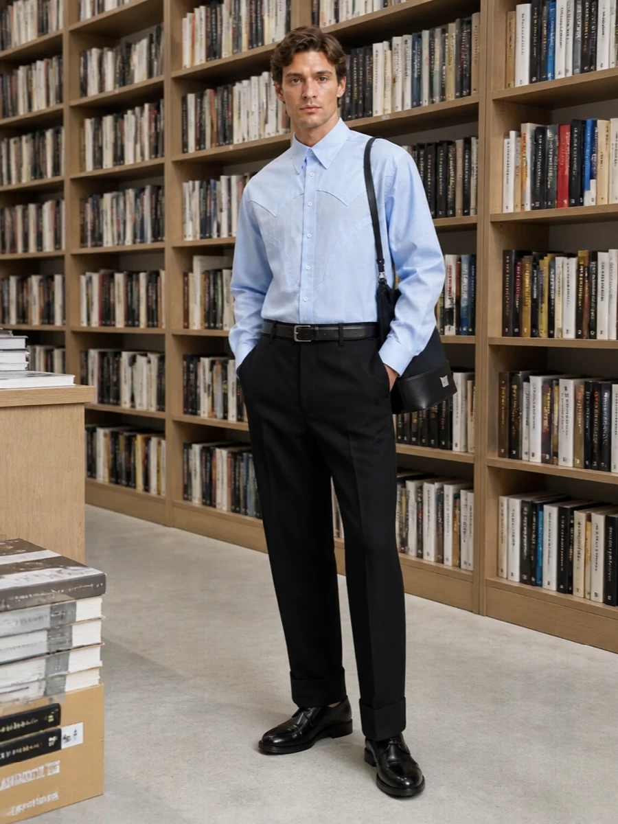 Pale blue Margiela shirting is anchored by a relaxed black tailored trouser for a clean, quietly formal base. Polished black derbies and a slim black belt keep the line sharp, while the structured black shoulder bag adds subtle Margiela attitude without disturbing the restrained palette. The result is a precise, office-ready ensemble that still feels soft and modern in proportion.
