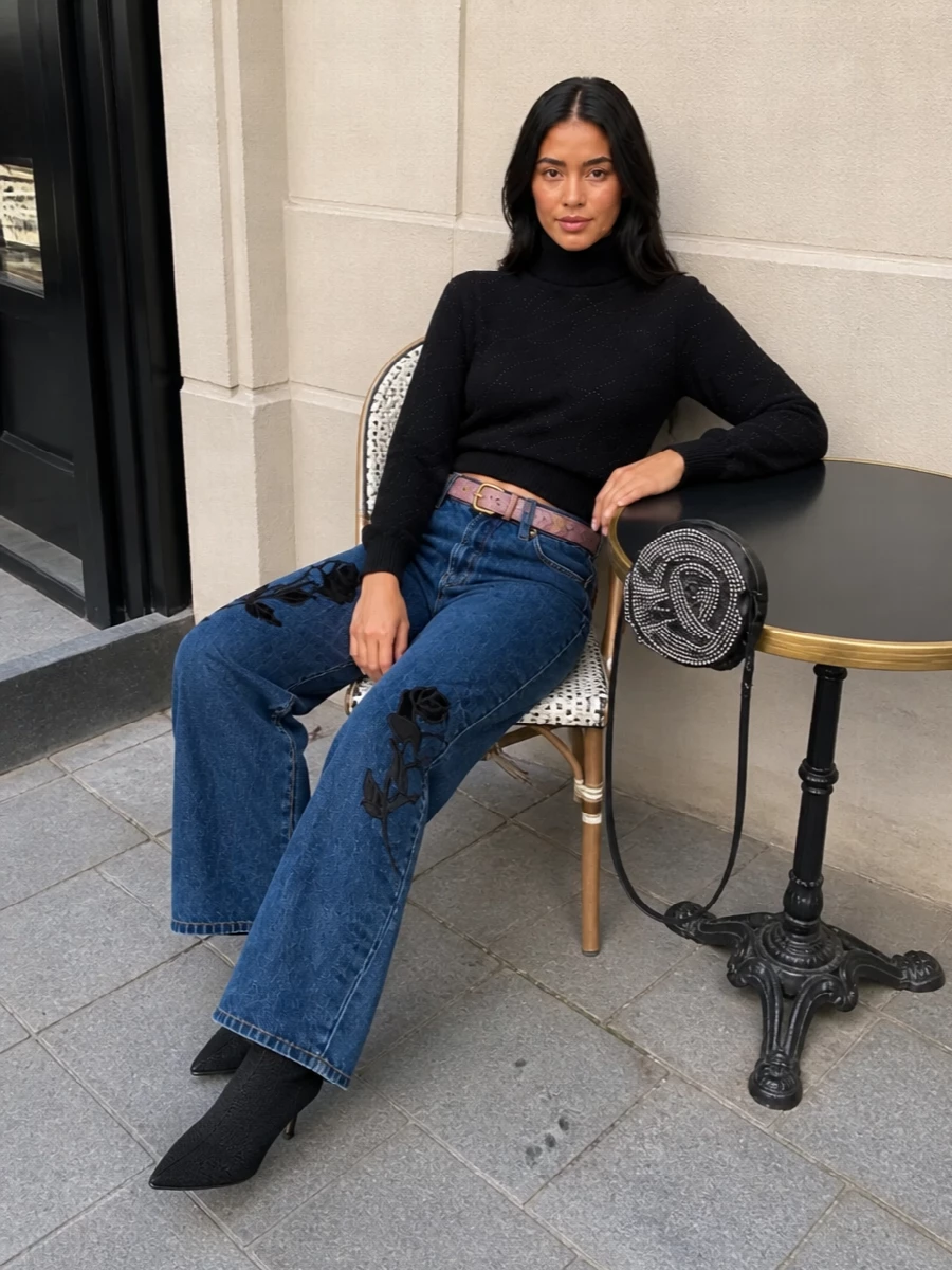 Darkly romantic denim goes nocturnal here, with the embroidered wide-leg jean grounded by a cropped black turtleneck and sleek sock boots. A dusted-rose belt and rhinestone rose pouch add just enough softness and shine, keeping the focus on the floral motifs and long, leggy line. It is a city-night take on Blumarine drama that feels sharp, feminine and unapologetically Y2K.