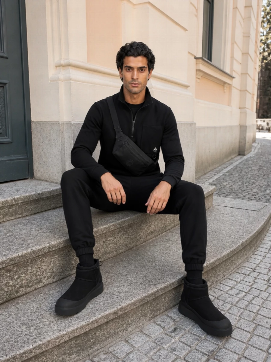 Moose Knuckles on top with tapered joggers, a chunky Ugg boot and a Moncler belt bag creates a tight, all-black street-sport uniform that feels ready for cold city movement. Technical details and subtle logos line up, so the outfit reads intentional rather than lounge, even though everything is built for comfort. The result is a modern winter set that goes from commute to weekend without any changes.