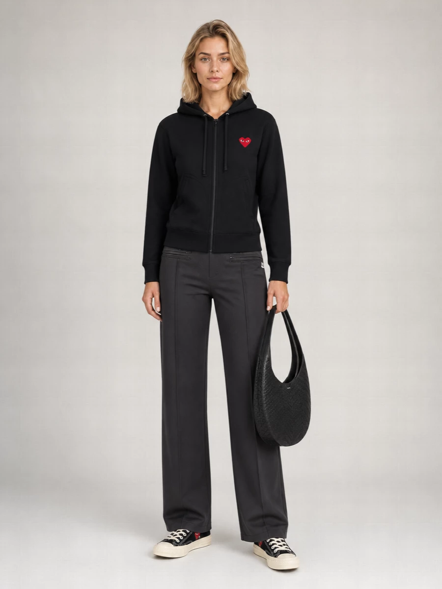 A black Play zip hoodie and sleek charcoal Courrèges track pants create a clean, sport-informed base that feels intentional rather than loungey. Black Play low-top sneakers continue the graphic story at ground level, while Coperni’s sculpted black shoulder bag and a quiet logo sock keep the palette tight and the styling thoughtful for city days on the move.