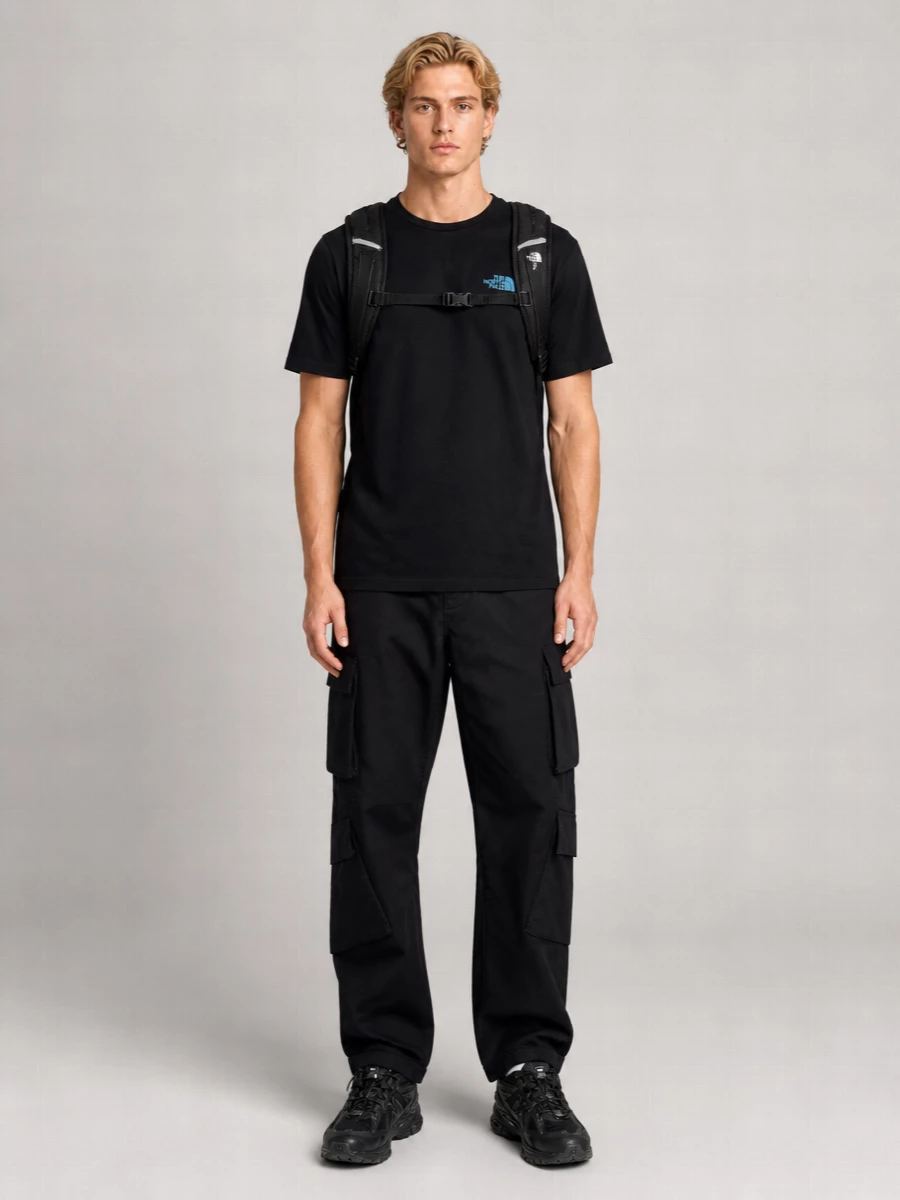 A black North Face tee with teal branding drops into structured black cargos for a clean, city-ready utility base. All-black New Balance trail runners and a technical Borealis backpack keep the mood practical and grounded without breaking the dark, minimal palette. It is an easy uniform for cold-season errands, travel days and low-key streetwear moments that still feel considered.