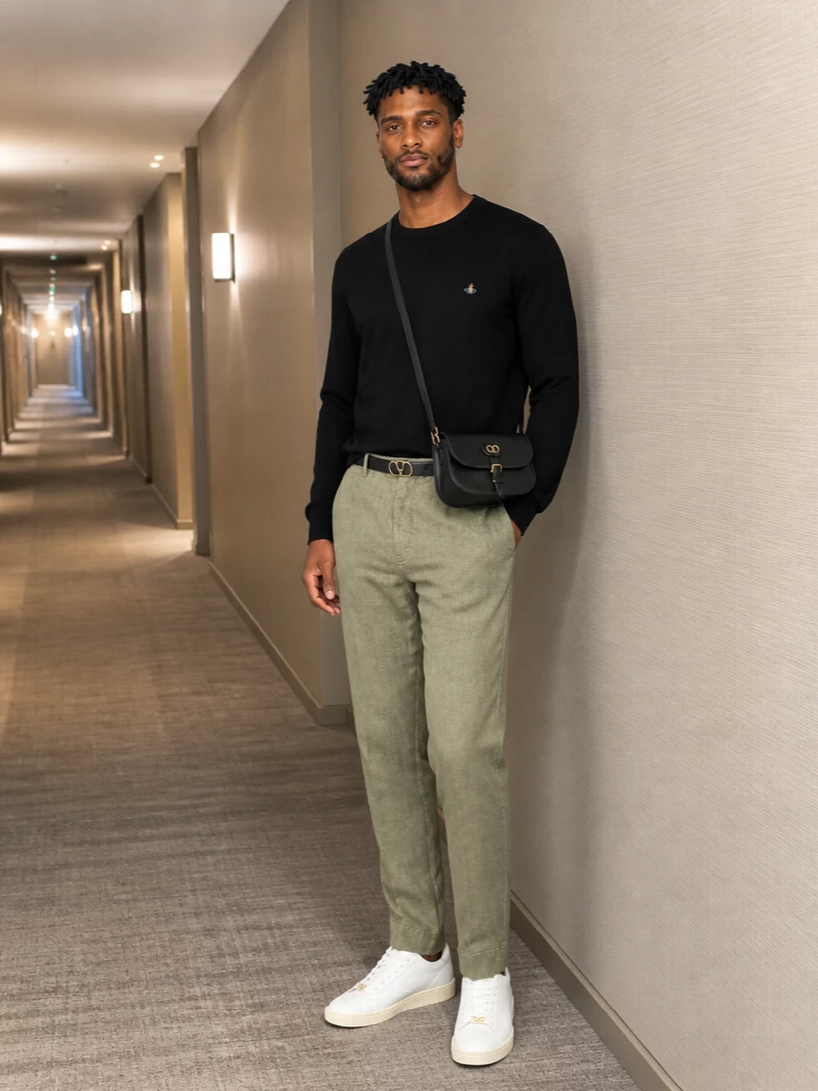 A black Orb-knit anchors the outfit against muted sage tailoring, giving that precise Vivienne Westwood attitude without shouting. Off-white Valentino sneakers keep the mood relaxed yet polished, while a slim black crossbody and belt in matching gold hardware quietly frame the silhouette. The result is a clean, modern combination that moves easily from late brunch to a low-key dinner in spring light.