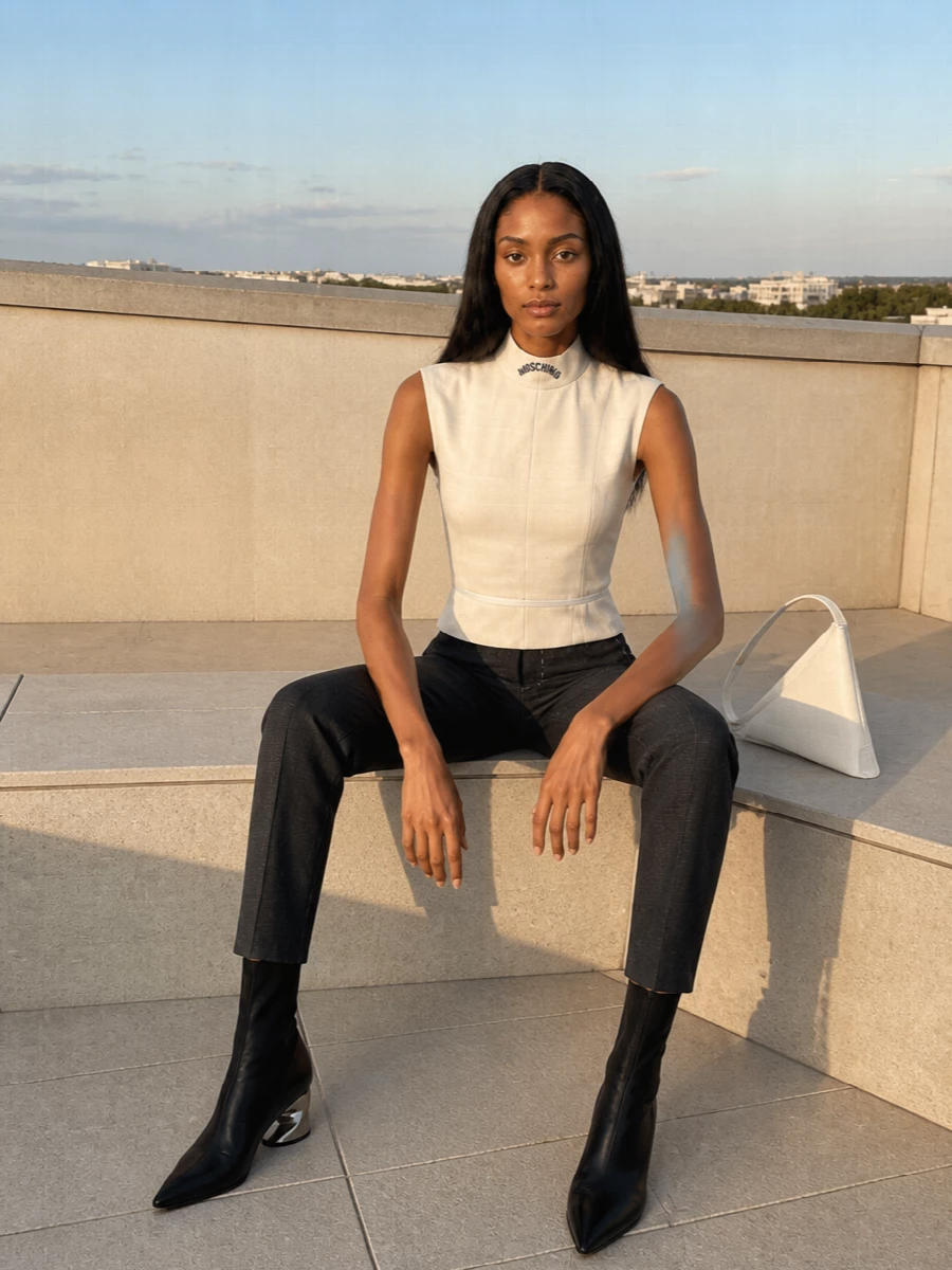 A sculpted cream mock neck meets high-waisted tapered charcoal trousers for a refined, elongated silhouette. Pointed black sock boots keep the line razor sharp, while the white geometric shoulder bag brings a subtle gallery-level twist. The result is minimal, precise and quietly commanding for evening tailoring or dressed-up city nights.