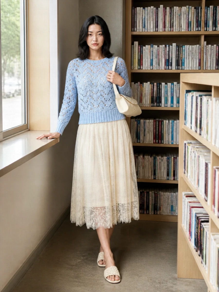 Powder blue and buttercream create a soft, luminous pairing, with the open-knit jumper layered over a flowing lace midi for quiet, romantic ease. Cream crochet slides and a structured buttercream shoulder bag keep the silhouette light and polished while letting the textures do the talking. A gauzy ivory and icy-blue scarf adds a final veil of softness around the face without disturbing the calm palette.