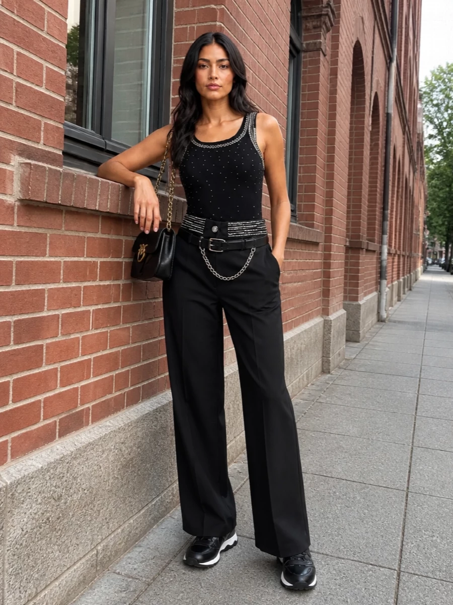 Pinko’s crystal-trim tank meets its match in high-waisted, silver-detailed wide-leg trousers for a clean, column line that feels club-ready yet confident. A quilted black shoulder bag and a hardware-rich belt keep the focus on a sharp black and silver story, with glossy sneakers pulling the whole thing into modern streetwear territory.