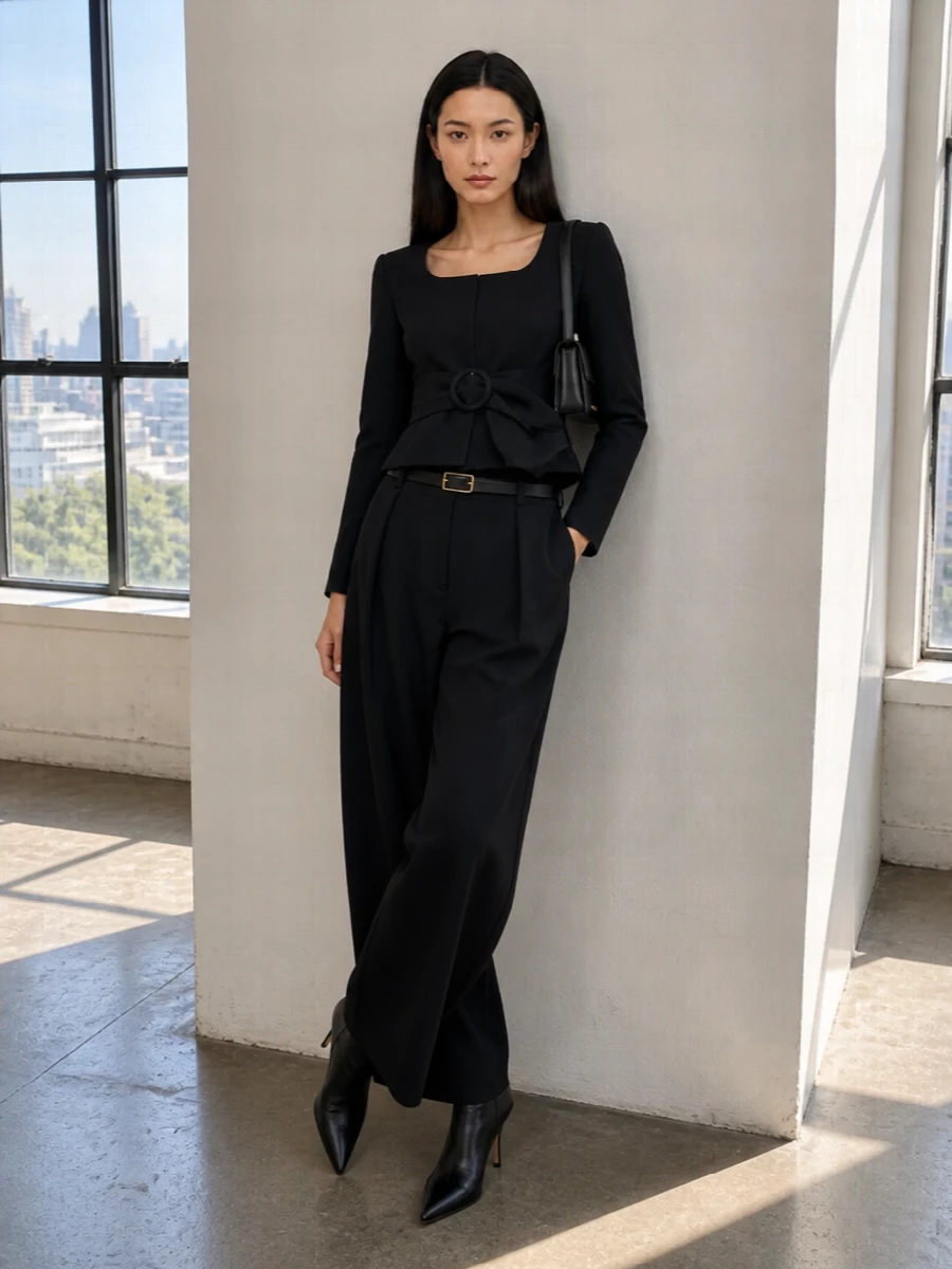 A sharply cinched black peplum jacket meets fluid high-rise wide-leg trousers for a sculpted, monochrome take on evening tailoring. Sleek pointed ankle boots and a slim black shoulder bag keep the lines uninterrupted, while a fine gold-buckled belt adds just enough hardware to underline the precision of the waist.