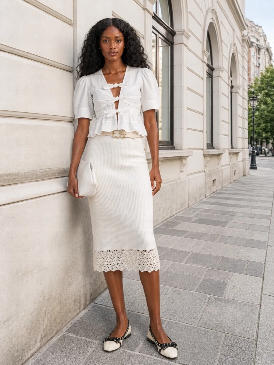 A soft white tie-front blouse meets an ivory knit skirt for a romantic, light-toned pairing that feels as easy as it is considered. Cream and black ballerinas keep it grounded and city-ready, while a blush clutch and nude belt add just enough structure and polish for daytime dates or relaxed dinners. The result is feminine, flattering and quietly confident without tipping into fussiness.