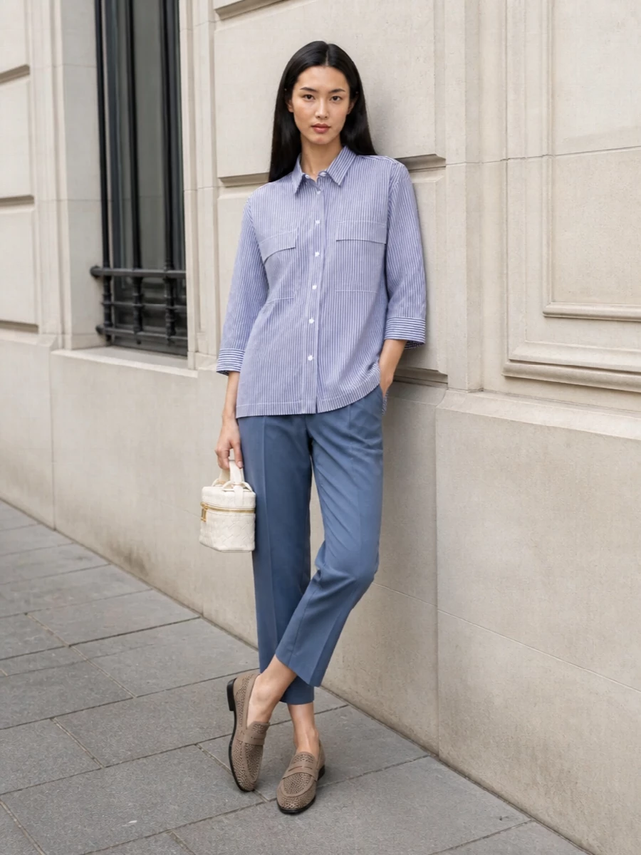 A longline striped Brunello shirt is paired with slate-blue tailored crops for a tonal, elongated silhouette that feels effortlessly sharp yet easy. Perforated taupe loafers and a small ivory intrecciato bag keep the mood light and minimal, finishing the look with quiet, high-luxury refinement that moves seamlessly from office to off-duty in SS.