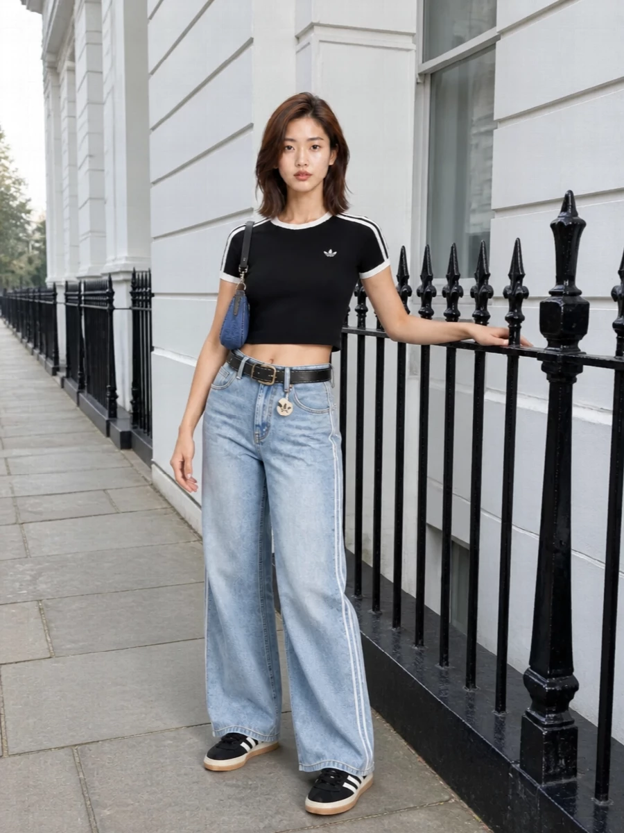 High-rise light-wash denim meets a sharp black crop and matching gum-sole sneakers for a clean, sporty Y2K mood. The slim top against the wide leg keeps the silhouette long and easy, while layered Adidas details and denim textures tie everything into one clear streetwear story. The compact denim shoulder bag finishes it with a nod to early‑2000s attitude without crowding the shape.