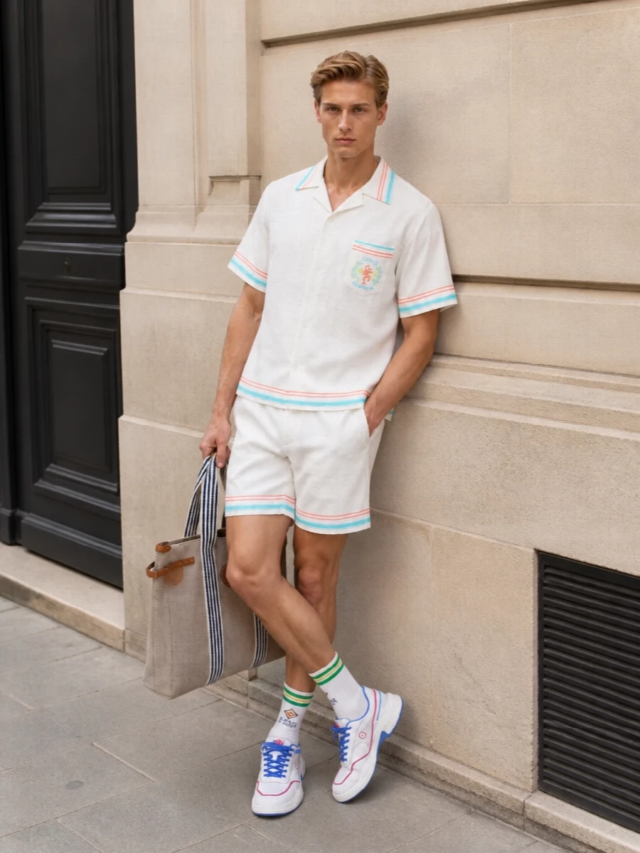 This look builds a refined resort set around the Casablanca shirt, pairing it with matching white deck shorts that echo its aqua and coral striping for a clean, coordinated silhouette. White court-inspired sneakers and striped athletic socks keep the mood sporty-preppy, while the beige canvas tote introduces a nautical touch that still feels light and polished for SS city or coastal days. The result is sunlit, easy, and unmistakably Riviera without ever feeling over-styled.