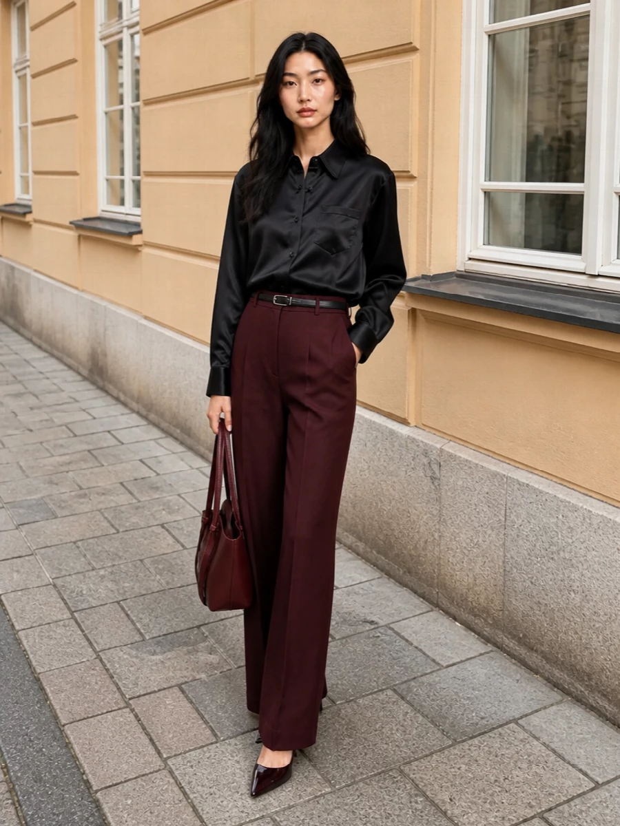 Deep burgundy tailoring meets a sleek black satin shirt for a refined, columnar silhouette that reads modern and assured. Oxblood heels and a sculpted matching bag stay within the same moody palette, adding depth without noise. A slim black belt is the only line of contrast, giving just enough definition at the waist while keeping everything clean and quiet.