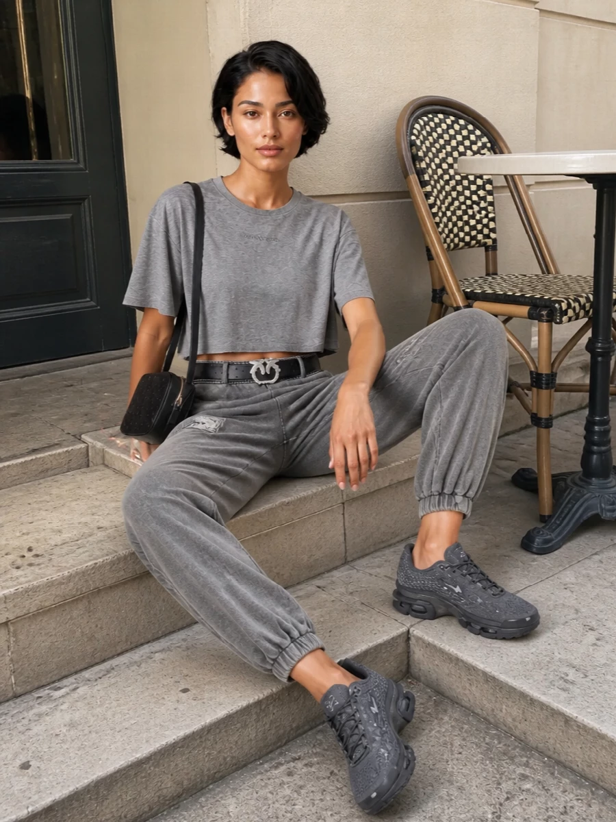 A washed-charcoal jogger meets a cropped heather tee for a monochrome, off-duty set that feels easy but intentional. Technical charcoal runners keep the palette tight and the mood athletic. A compact black crossbody and a clean belt add just enough structure so the greys read styled rather than thrown on.