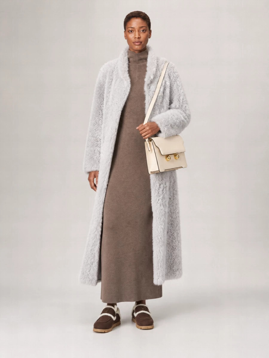 I am keeping this as a knit-column story, pairing the long grey faux-fur coat with a taupe Max Mara maxi dress rather than breaking the line with separate top and trouser. The result is a quiet, elongated silhouette in soft neutrals, anchored by dark chocolate shearling mules and a structured cream shoulder bag for just enough definition. It feels like winter cocooning translated into city polish, tactile but very controlled.