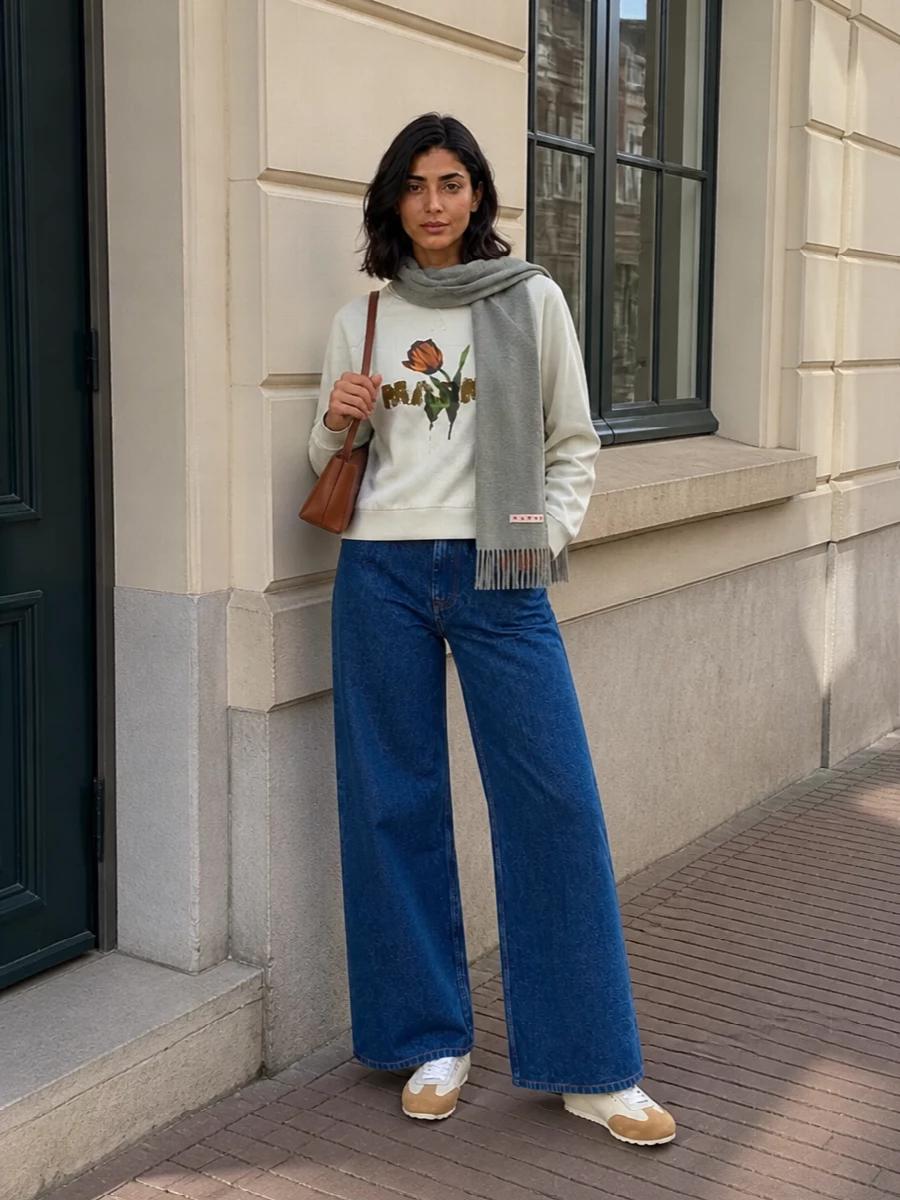 Softly graphic on top and column-clean through the leg, this pairing keeps Marni’s tulip print grounded in pure, straight-lined denim. Cream and tan accents in the sneakers and shoulder bag thread through the warm notes of the graphic, while the sage scarf echoes the sweatshirt so the whole palette feels calm, modern and pulled together for off-duty city days.