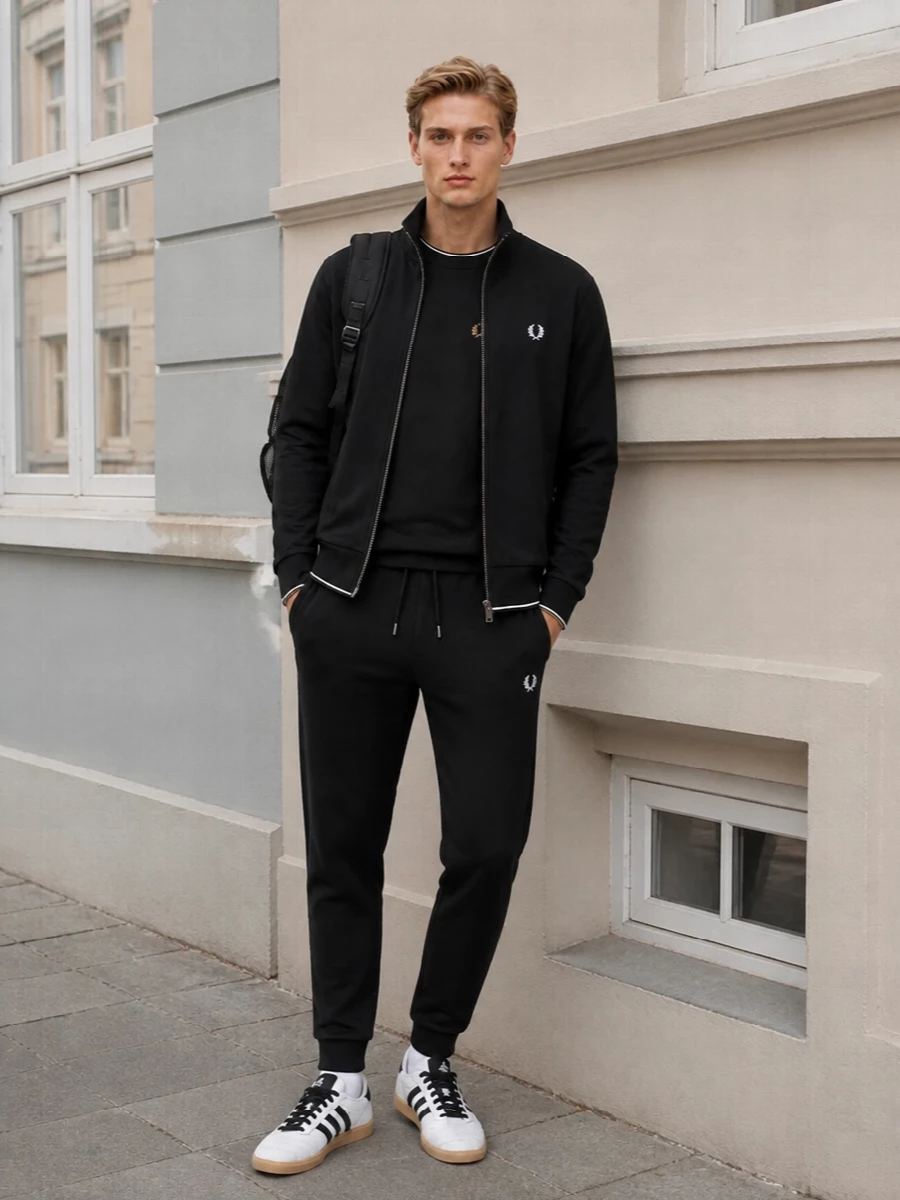 Head to toe terrace energy in a strictly monochrome story, anchored by Fred Perry trackwear and finished with classic Adidas gum sole sneakers. The tapered jogger and neat crew keep the proportions sharp under the clean black jacket, while the technical backpack leans it toward everyday city movement rather than pure gym kit. It is an easy, confident uniform for cold-season commutes, matches or weekend runs around town.