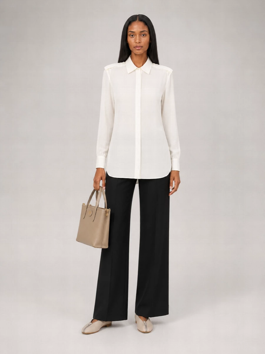 An ivory longline shirt falls over precise black wide-leg tailoring for a clean, elongated take on modern power dressing. Light-beige flats keep the line refined but unfussy, while a structured taupe top-handle adds a decisive, boardroom-ready finish without tipping the palette into hardness.