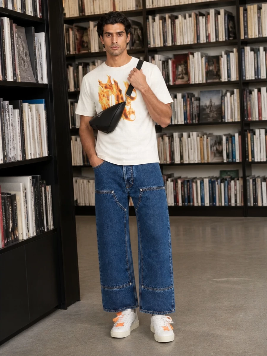 The flaming Palm Angels tee sits over wide-leg indigo denim for a clean, skate-led line that lets the graphic do the talking. Low-profile Off-White court sneakers pick up the orange from the print, while the black Prada crossbody and striped socks keep everything tight and technical without cluttering the silhouette. It is a confident city uniform that balances strong branding with an easy, relaxed shape.