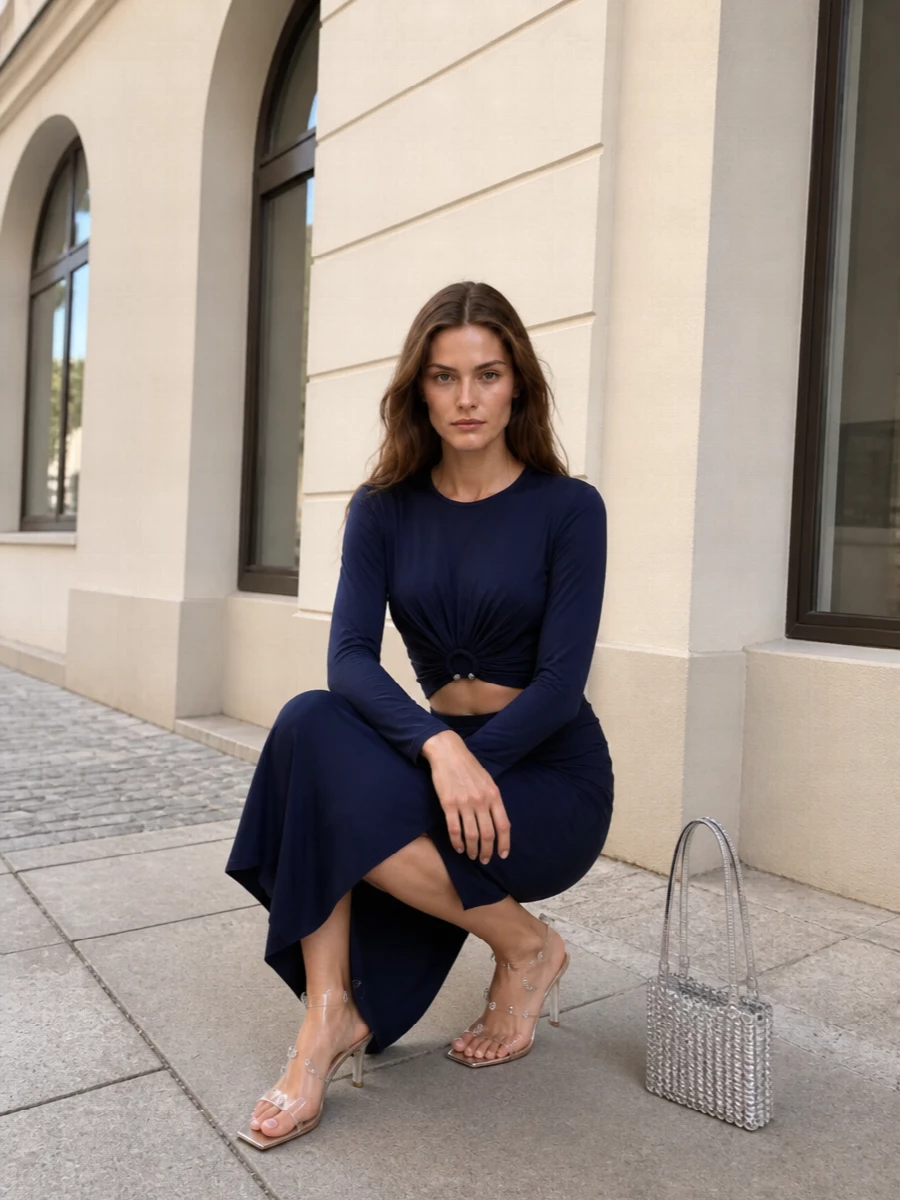 Midnight navy and silver play quietly off each other here, with the twisted crop and draped midi reading as a modern, almost gown-like column. Barely-there crystal Plexi sandals and a silver chainmail shoulder bag keep the mood polished and romantic, catching light without competing with the fluid silhouette. The gauzy navy wrap finishes it with softness and a discreet shimmer for warm summer evenings out.