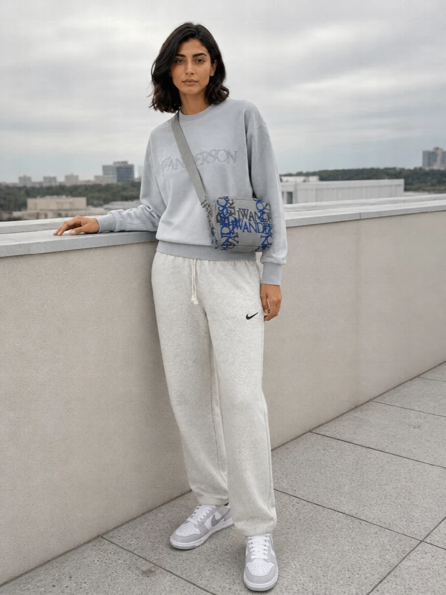 A soft gradient of greys keeps this off-duty set feeling calm and clean, from the ombré logo sweatshirt down to the matching marl track pants. White and grey sneakers keep the line sporty and light, while the graphic crossbody and heather scarf add just enough interest without disturbing the monochrome mood. It is relaxed airport-to-weekend dressing that still feels considered and coherent.