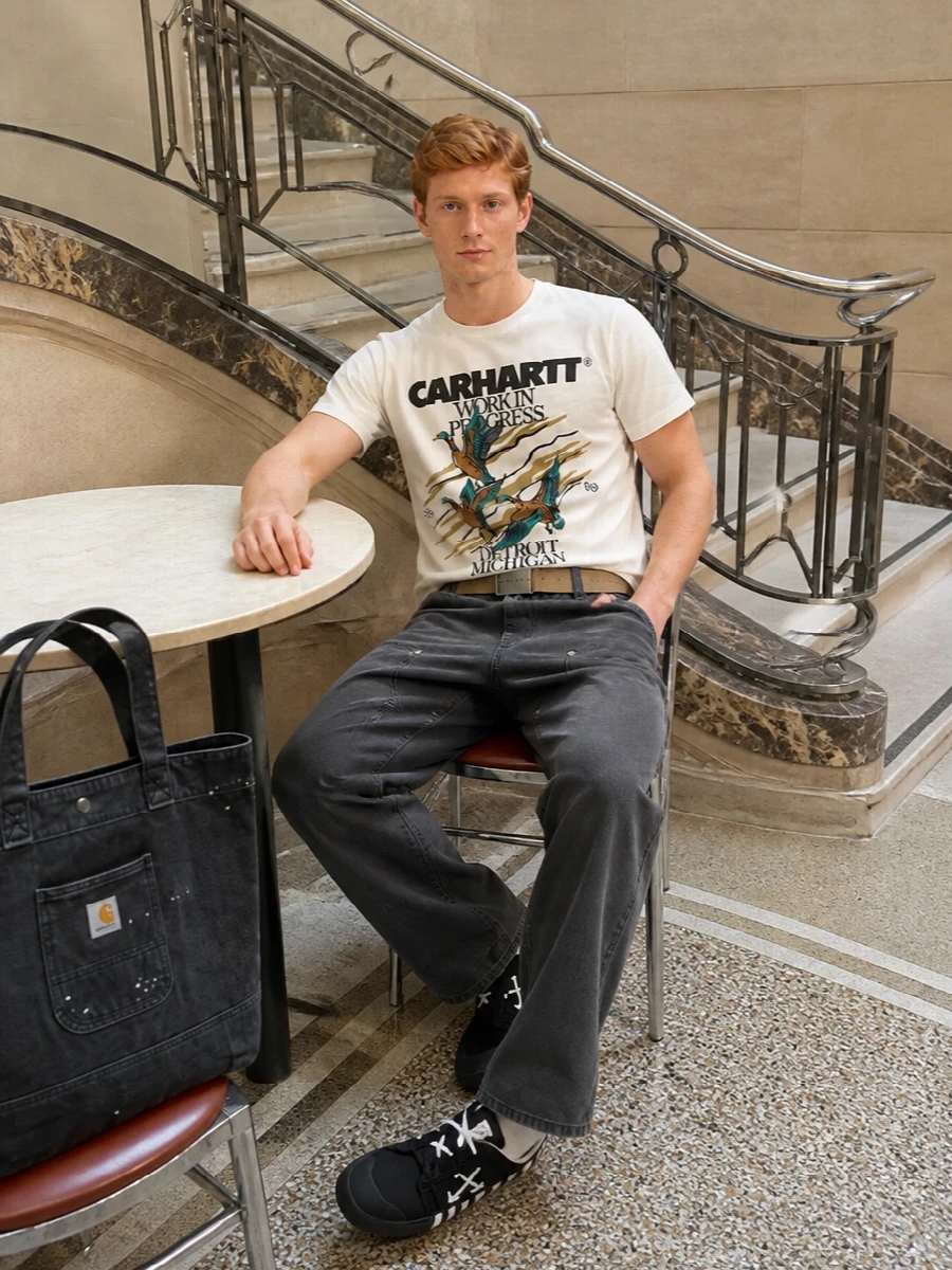 Carhartt WIP’s duck graphic tee sits on washed charcoal work pants, keeping the palette muted so the artwork really carries the attitude. The Off-White canvas sneakers sharpen it just enough, while the paint-splattered denim tote and sand webbing belt lean into that lived-in, utility-first street feel without overcomplicating the silhouette. It is an easy, straight-cut uniform built for city days where comfort and character matter equally.