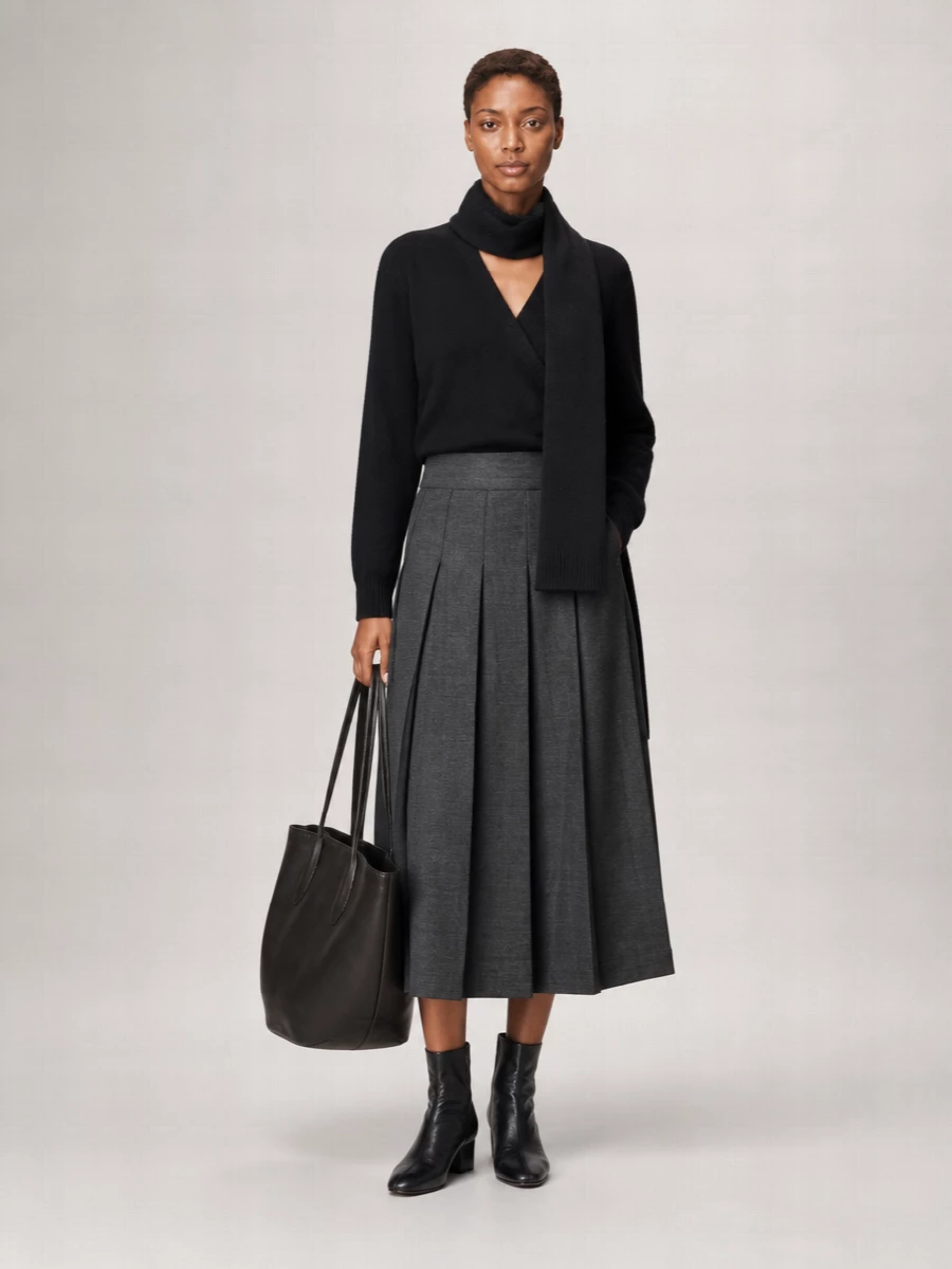 Róhe’s black wrap knit meets a high-rise charcoal wide leg for a calm, tailored silhouette that feels considered from desk to late dinner. The soft pleats and pooled hem create an elongated column, kept sharp by almost-invisible black ankle boots. A sculpted black tote and matching knit scarf finish the outfit with quiet structure and depth in a strictly monochrome register.