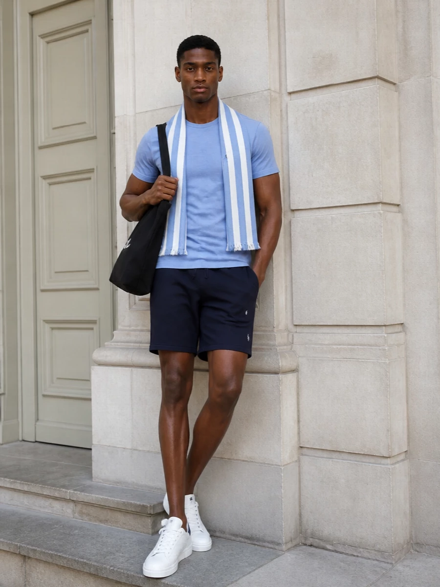 Soft light blue on top and deep navy below sets a clear, easy palette that feels fresh without trying. White court sneakers keep the line clean and sporty, while the black canvas tote adds just enough city sharpness. The striped scarf brings a hint of seaside character you can use or stash depending on the day.