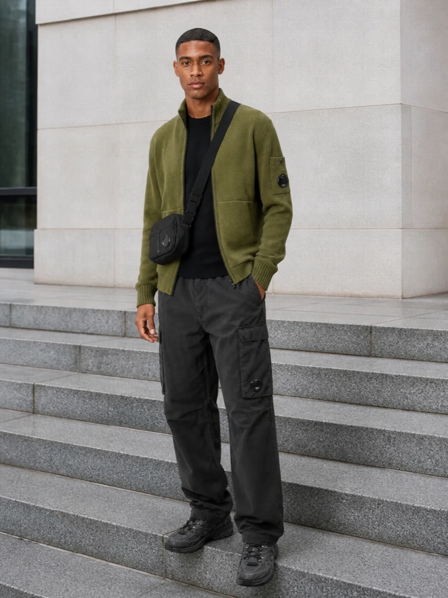 Olive and charcoal keep this C.P. Company outfit firmly in the technical utility lane, with the knit zip jacket sitting clean over a dark crew base. Charcoal cargos and monochrome Salomon runners ground the palette, while the compact crossbody quietly repeats the lens detailing. The result is a streamlined city uniform built for movement, not noise.