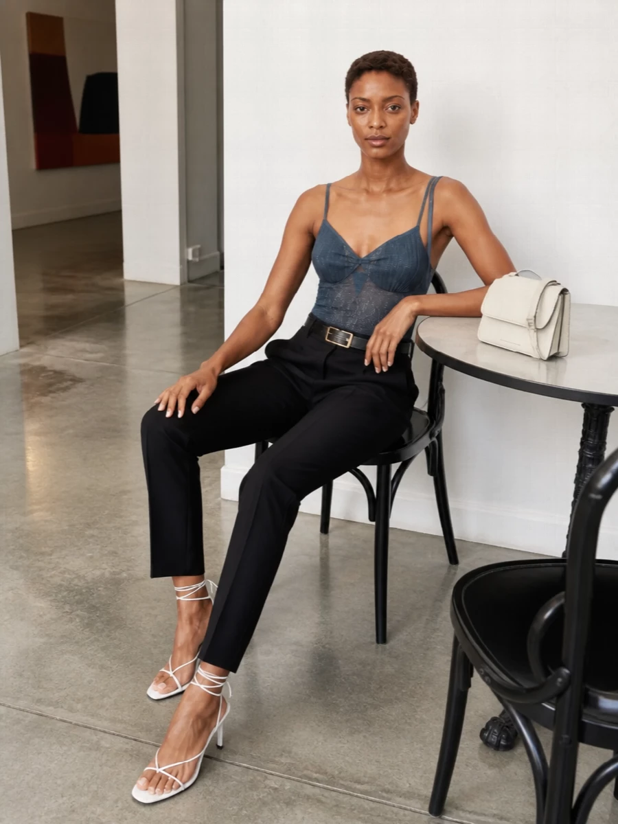 An ink-blue sheer tank meets precise black tailoring for a composed, quietly sensual evening ensemble. The pointed white sandal and ivory shoulder bag lighten the palette just enough, keeping everything graphic and modern. A slim black belt anchors the proportions so the transparency feels intentional and controlled.
