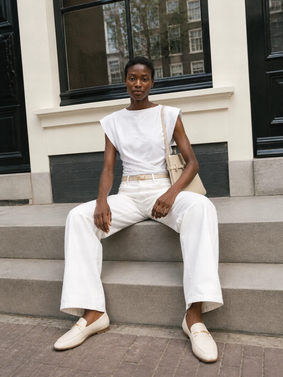 A clean white-on-white base lets the sculpted top and wide-leg denim do the quiet work, all in a soft neutral palette that feels calm and intentional. Ivory loafers and a cream shoulder bag keep the mood relaxed yet precise, while a slim white belt subtly anchors the high waist for a long, easy line. The result is polished day dressing that reads modern, minimal and quietly confident.
