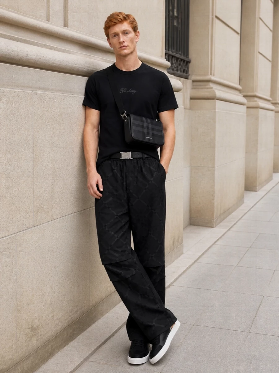 This look centres on the wide-leg jacquard Burberry track pant, paired with the tonal-logo black tee for a quietly elevated, monochrome streetwear statement. Sleek black-and-white Burberry sneakers keep the proportions crisp at the hem, while the structured tonal-check crossbody and technical-inspired belt add just enough refinement to push the outfit into modern quiet luxury without breaking its ease.