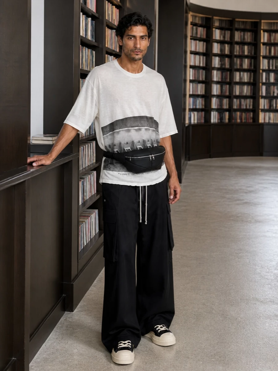 This is pure Owens uniform energy: the floor-grazing black cargos anchored by the elongated soft white graphic tee for a long, columnar silhouette. The iconic black and cream hi-tops and padded belt bag keep everything grounded and practical, with the striped socks adding a tiny sport note that does not break the monochrome tension. It reads dark, directional and easy for warm urban days when you want volume without noise.